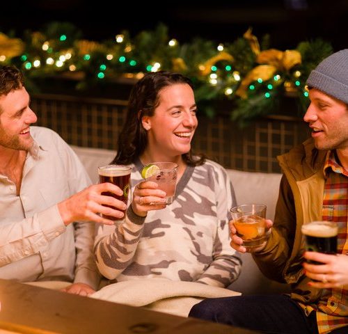 A group of happy guests at Limelight Hotel sitting by the fire- après-ski in the Limelight Lounge
